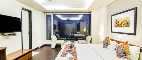 A hotel room with a bed, a TV, a desk, and a view of the outside.