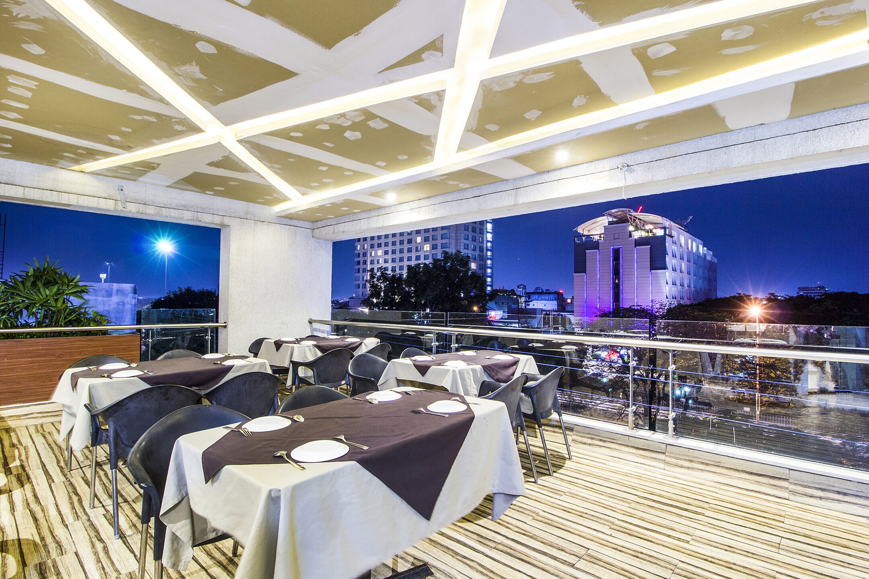 A rooftop restaurant with tables set for dining, overlooking a cityscape at night.