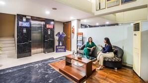 A lobby with a reception desk, a glass coffee table, a sofa, and an elevator. - Fabhotel Prime Avenue (Indore)