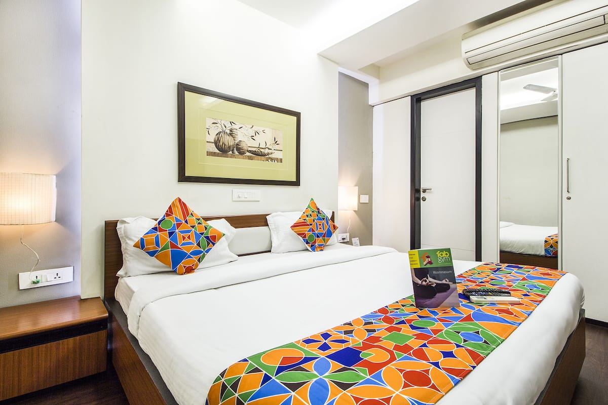 A hotel room with a bed, a nightstand, a lamp, a framed picture on the wall, and a wardrobe.