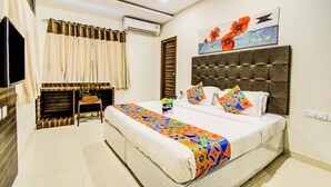 A hotel room with a large bed, a desk, and a chair. There is a painting on the wall and an air conditioning unit. - Fabhotel Pearl City (Hyderabad)