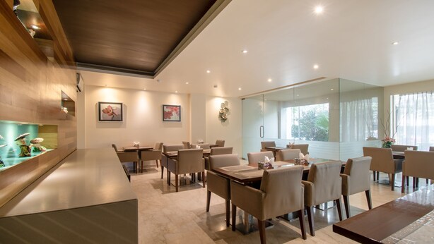 A modern dining area with multiple tables and chairs, a wooden accent wall, and artwork on the walls. - Treebo Cabana (New Delhi)