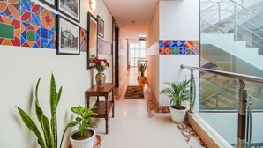 A hallway with a wooden bench, potted plants, framed pictures, and a staircase with glass railings. - FabHotel Marble Arch - Nr. Karol Bagh Market (New Delhi)