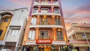 Un hôtel à plusieurs étages, reconnaissable à son grand panneau « Fabexpress » placé à l’entrée, doté de balcons et présentant un style architectural classique.