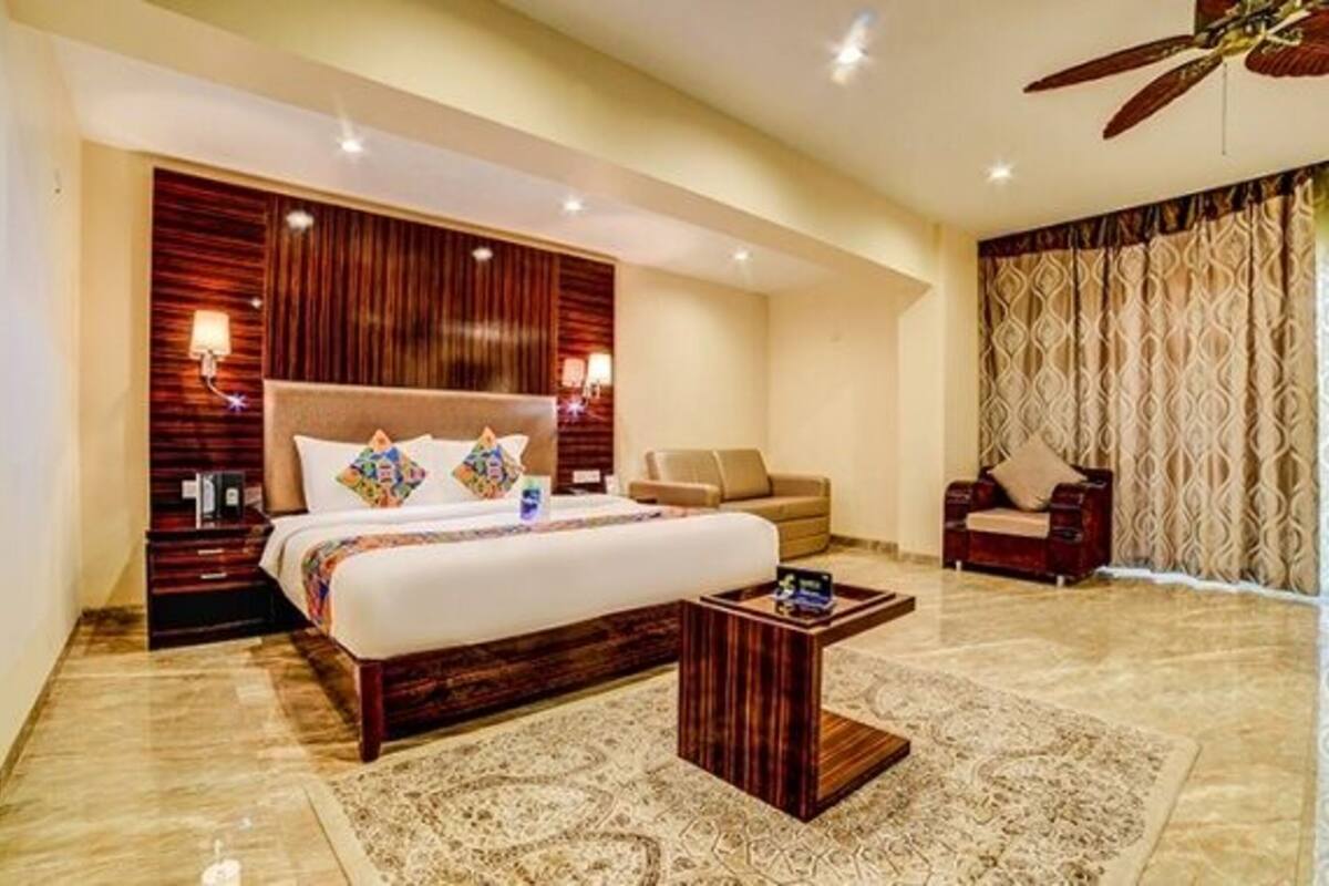 A hotel room with a large bed, a sitting area with a sofa, a small table, and a ceiling fan.