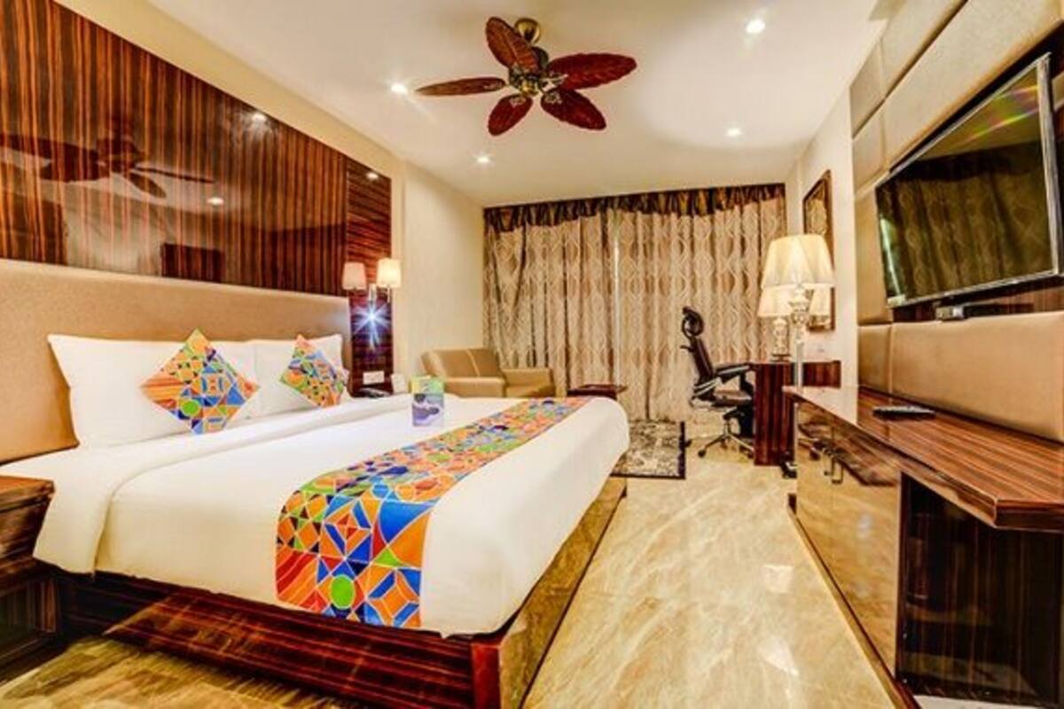 A hotel room with a large bed, a desk, a chair, a TV, and a ceiling fan.