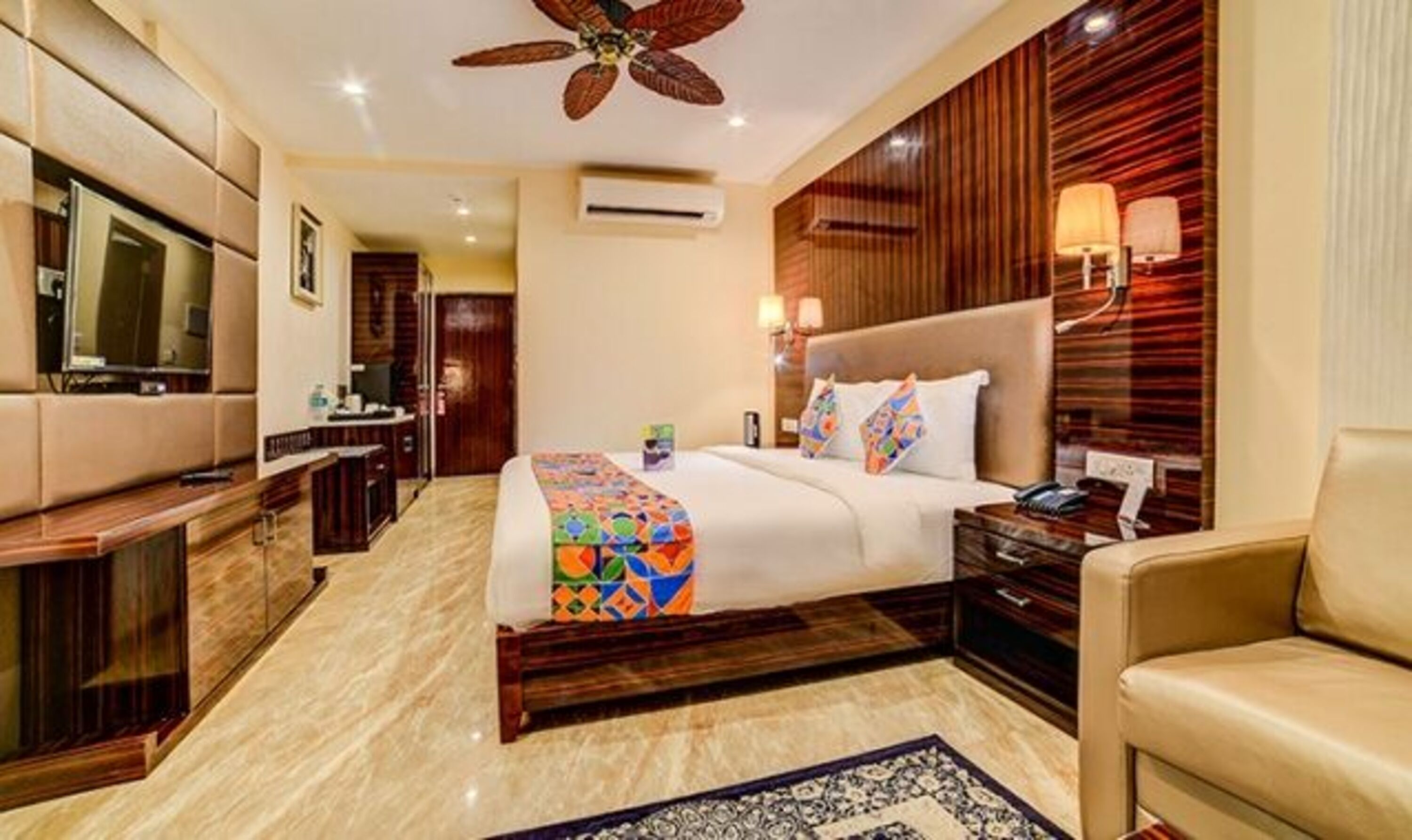 A hotel room with a bed, a desk, a TV, a ceiling fan, and a wooden wall panel.