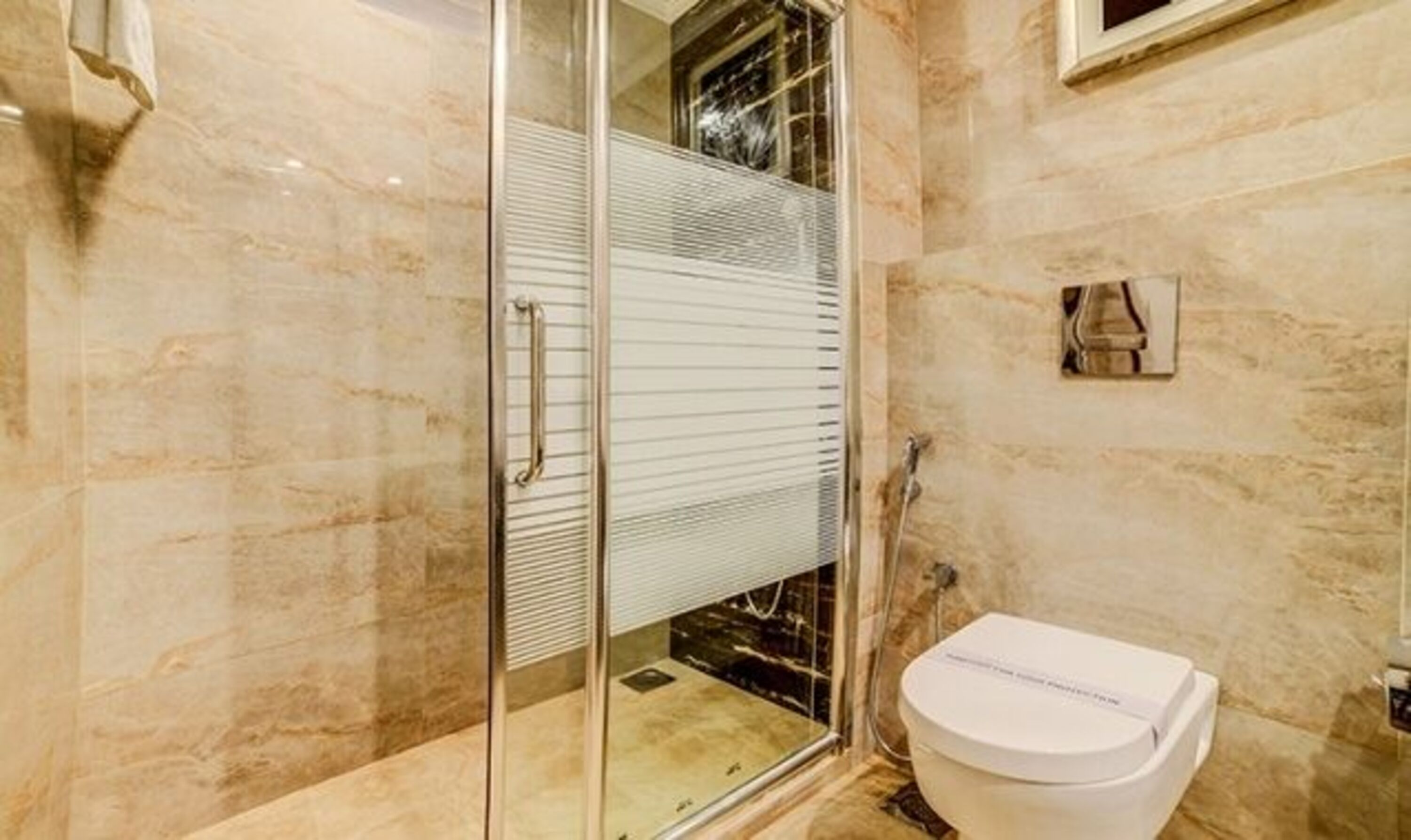 A bathroom with a glass-enclosed shower, a white toilet, and marble walls.