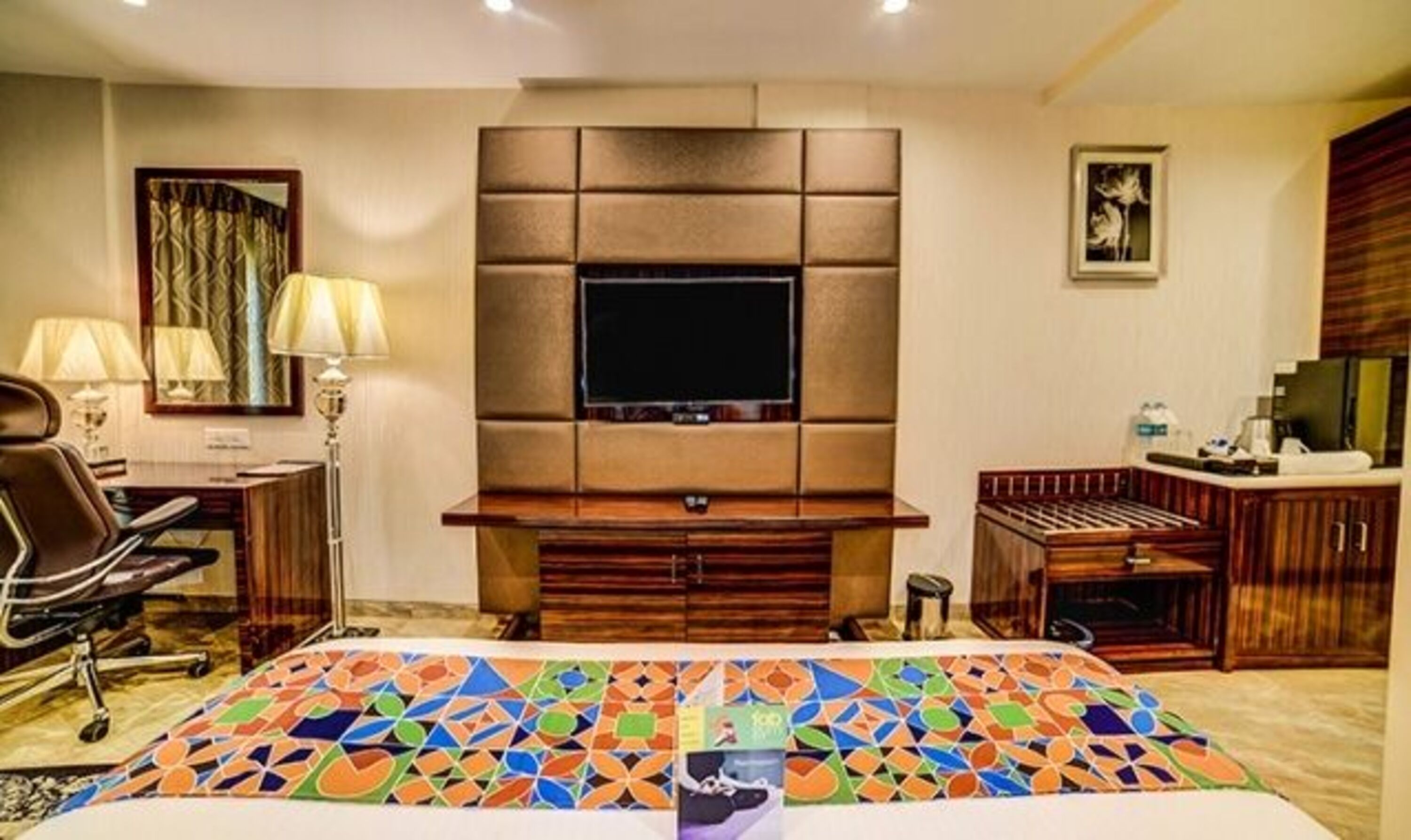 Habitació d'hotel amb un llit gran, una televisió muntada a la paret acolxada, un escriptori amb una làmpada i una petita zona de cuina.