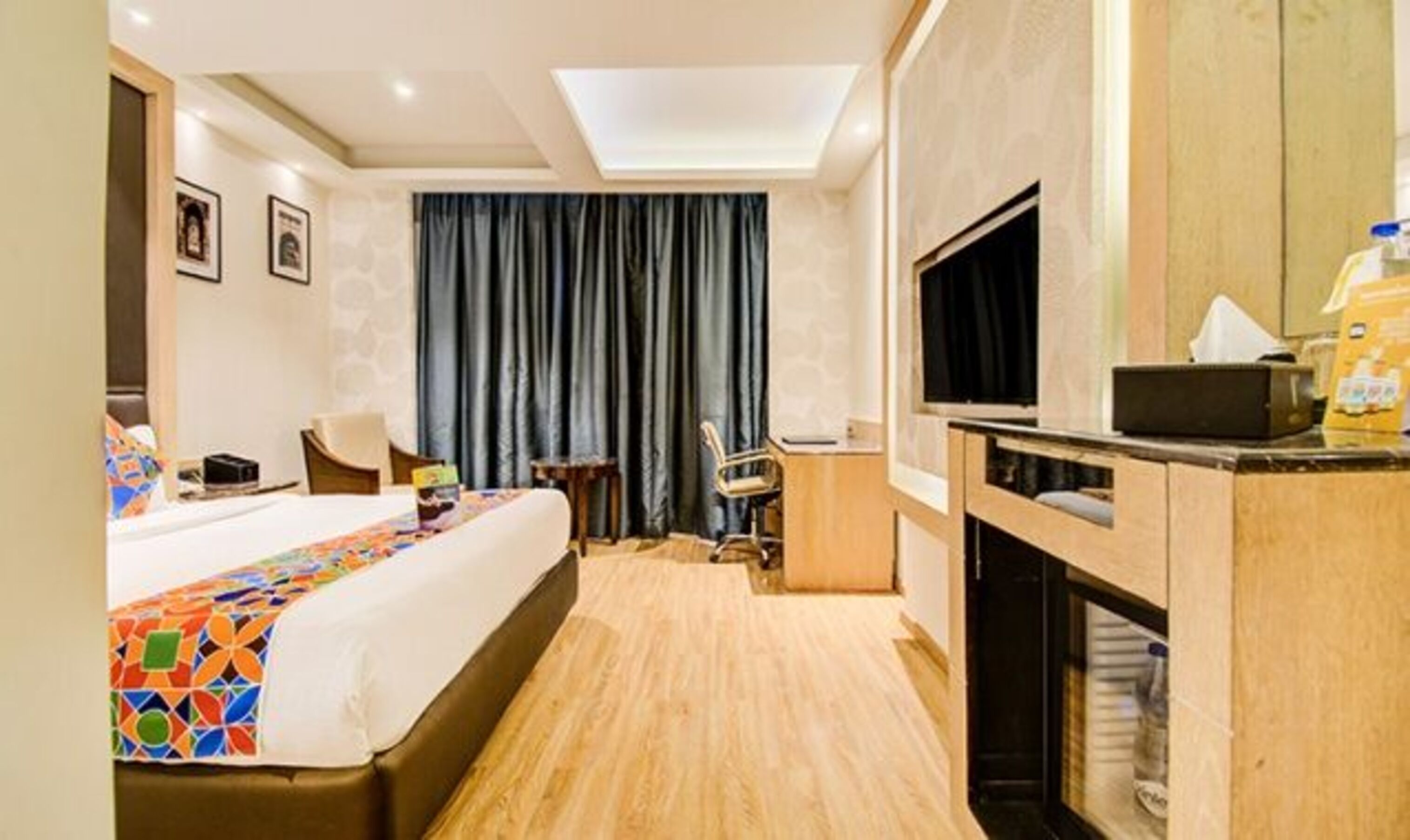Ein Hotelzimmer mit einem Bett, einem Schreibtisch, einem Fernseher und einem großen Fenster mit Vorhängen.