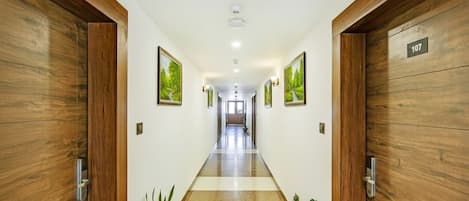 A hallway with wooden doors, potted plants, and framed pictures on the walls.