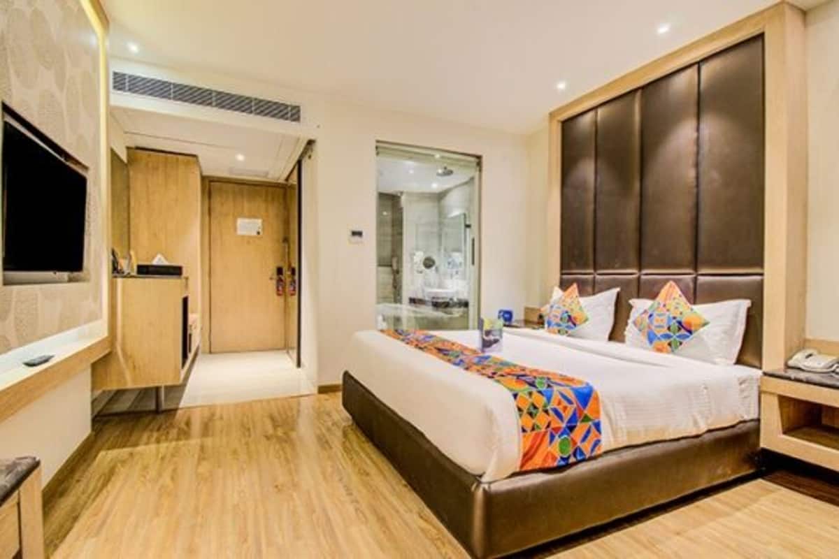 Habitación de hotel con una cama grande, un televisor montado en la pared, un escritorio de madera y un baño visible a través de una puerta de vidrio.