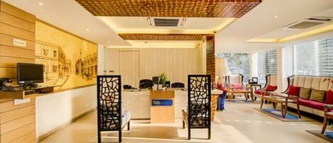 A modern hotel lobby with a reception desk, seating area, and large windows.