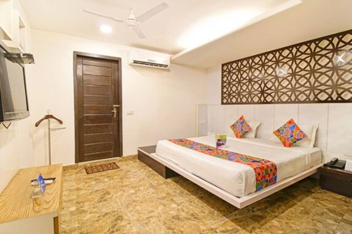 Una habitación de hotel con una cama, un ventilador de techo, una puerta de madera y un panel decorativo en la pared.