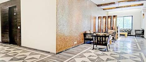 A spacious lobby with a geometric patterned floor, a seating area with a sofa and chairs, and a large wall with vertical panels.