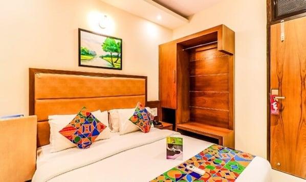 Una habitación de hotel con cama, almohadas, un cuadro, un armario de madera y una puerta.