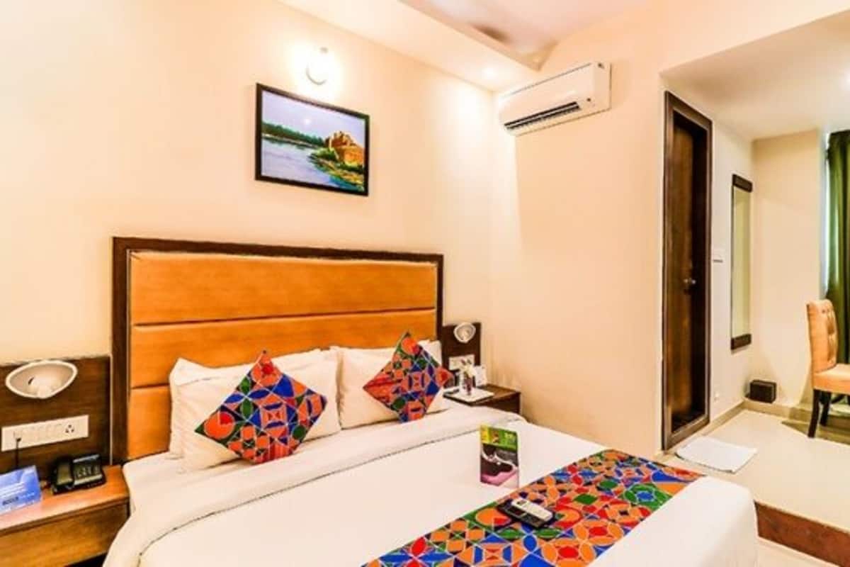 A hotel room with a bed, a nightstand, a chair, a television, and a door leading to another room.