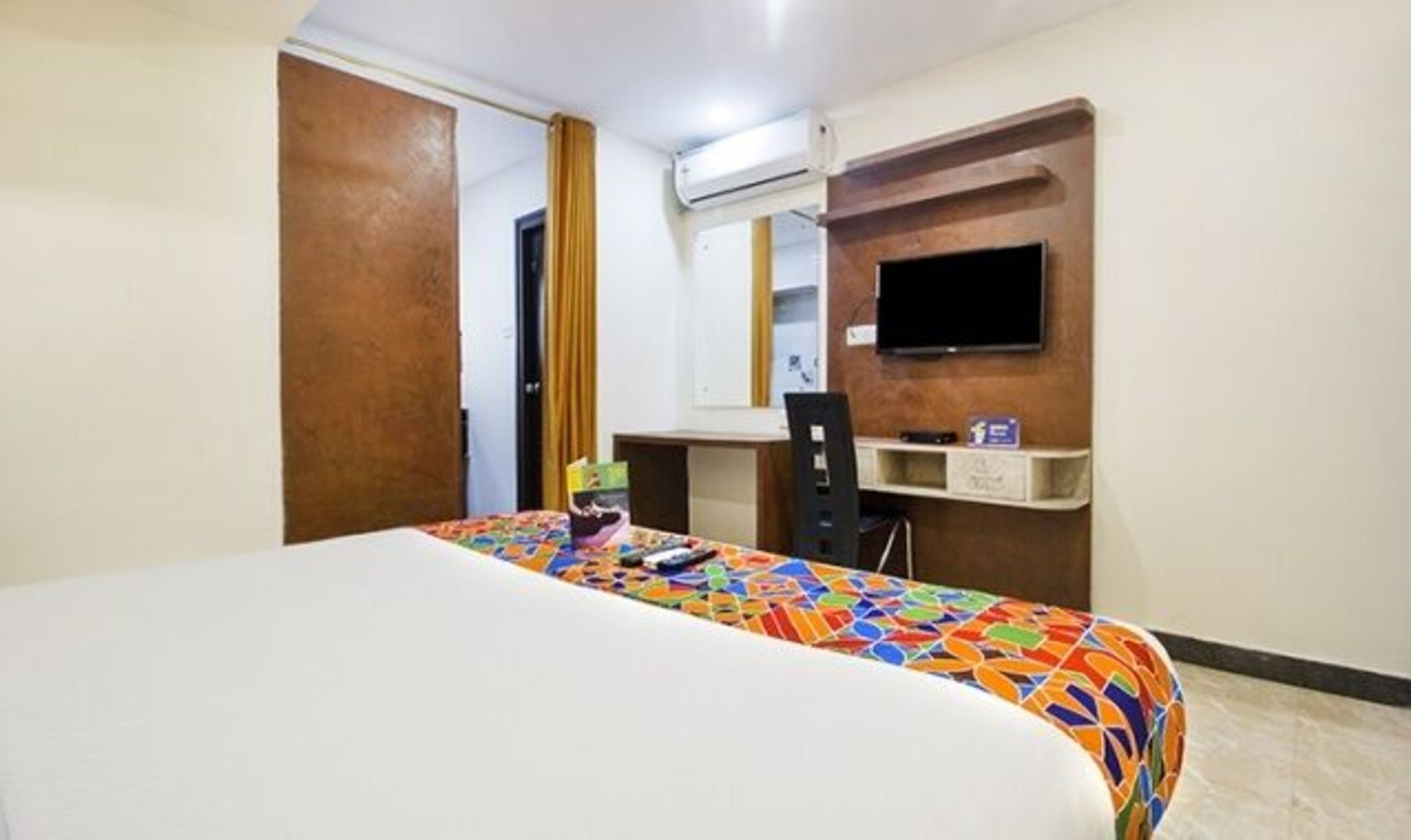 Una habitación de hotel con cama, escritorio, silla, televisión y un estante pequeño.