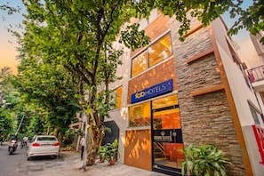 A hotel with a modern facade, a sign indicating 'Crown Suites,' and a street view with parked cars and a tree. - Fabhotel Crown Suites (Bengaluru)