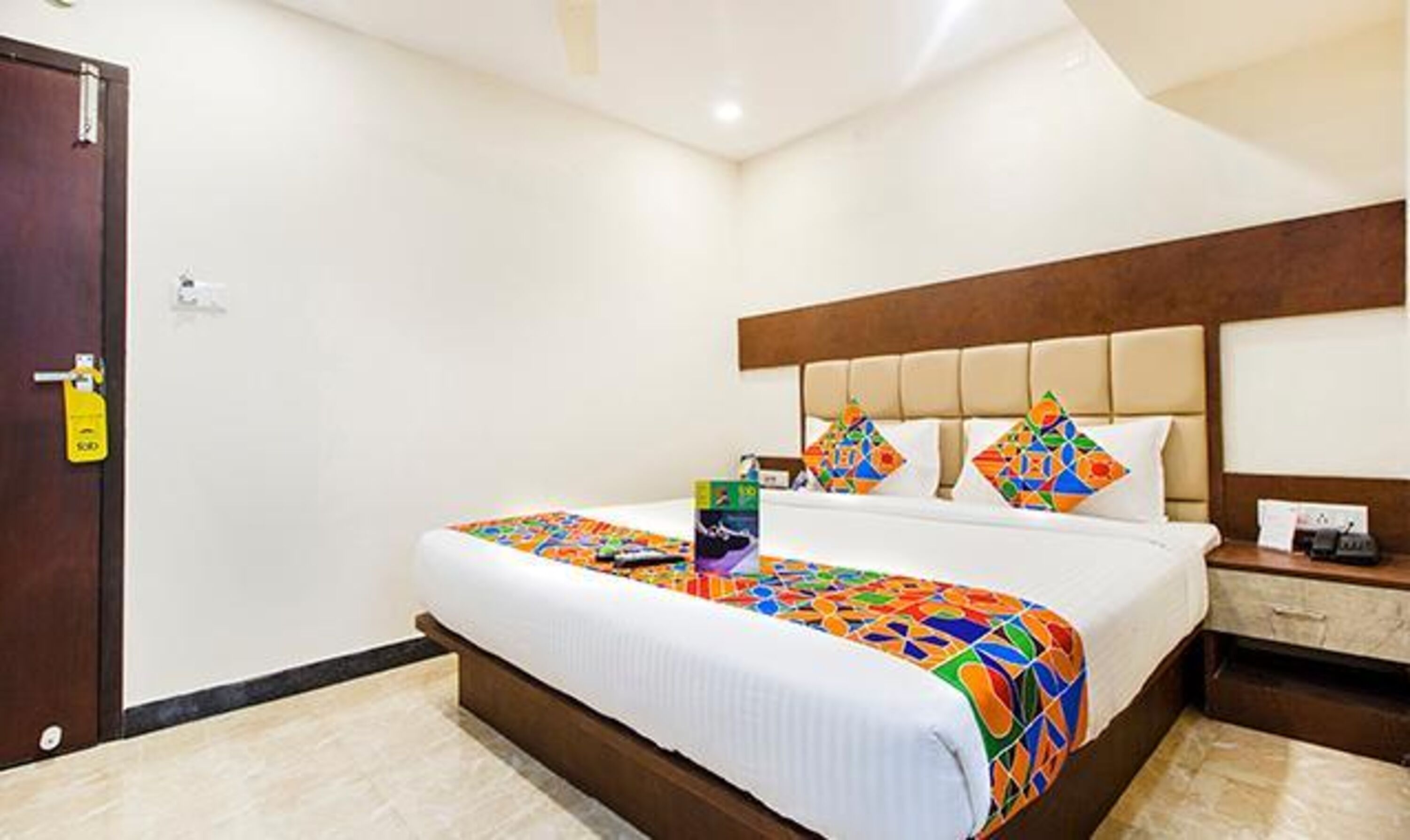 A hotel room with a bed, a nightstand, a door, and a wall-mounted light.