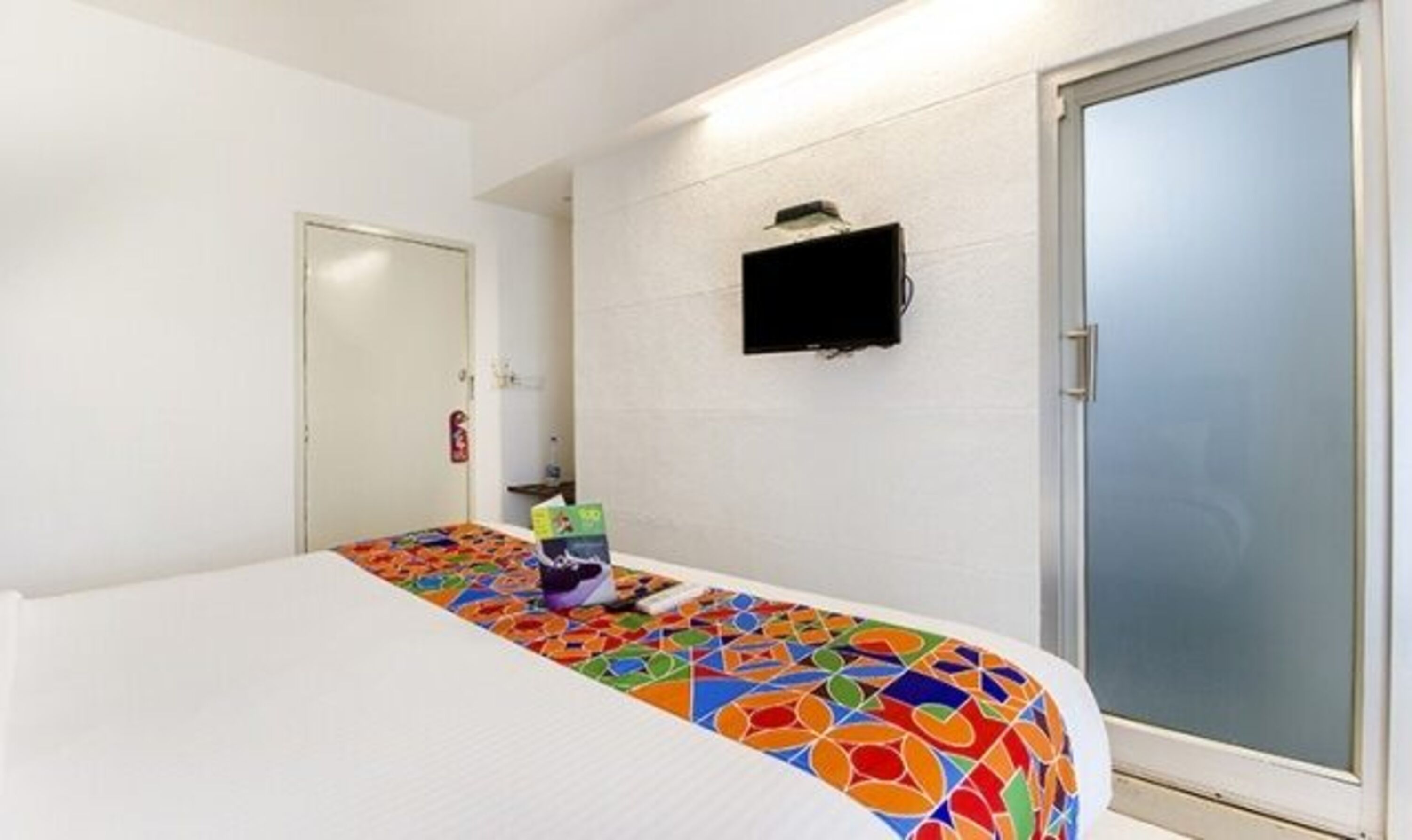 A hotel room with a bed, a TV mounted on the wall, and a sliding door.