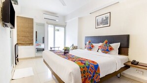 A modern bedroom with a large bed, a bedside table, a TV, and a window. - FabHotel Kalyan (Vadodara)