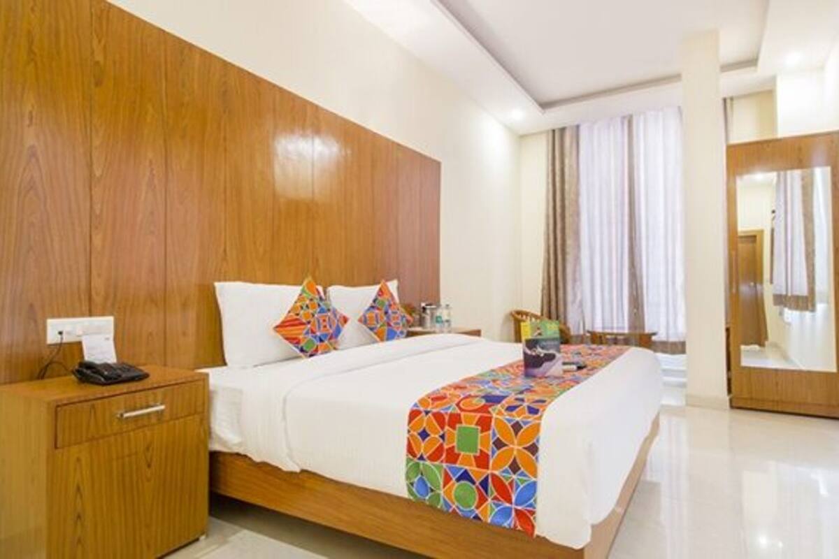 A hotel room with a wooden headboard, a bed with colorful bedding, a bedside table with a phone, and a mirror on the wall.
