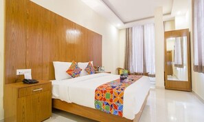 Une chambre d’hôtel avec une tête de lit en bois, un lit avec une literie aux couleurs vives, une table de chevet avec un téléphone et un miroir sur le mur.