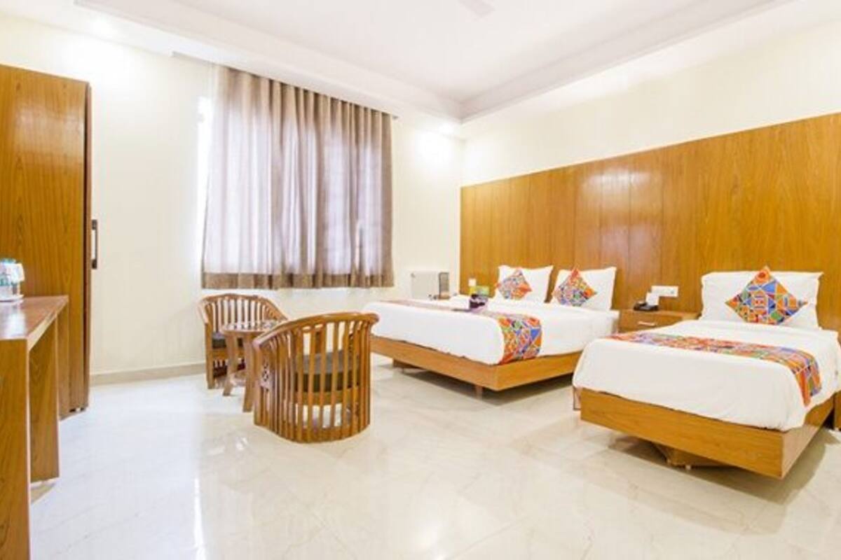 A hotel room with two beds, a wooden wardrobe, a desk, and a chair.