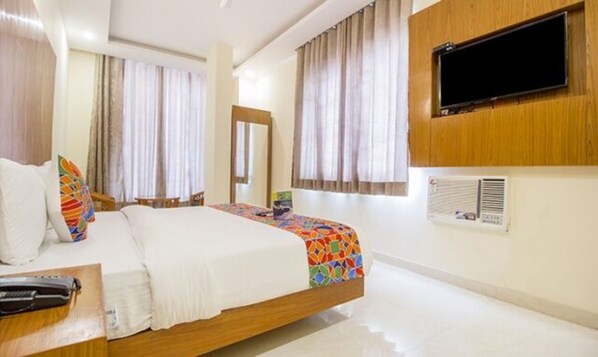 A hotel room with a bed, a TV mounted on the wall, and a window with curtains.