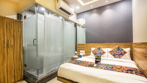 A hotel room with a bed, a wooden wardrobe, a glass shower enclosure, and a bedside table with a book and a bottle. - FabHotel Marol Metro (Mumbai)