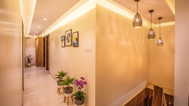 A hallway with a modern design, featuring a light-colored floor, a wooden door, and a wall with abstract art. There are potted plants and pendant lights. - FabHotel Marol Metro (Mumbai)