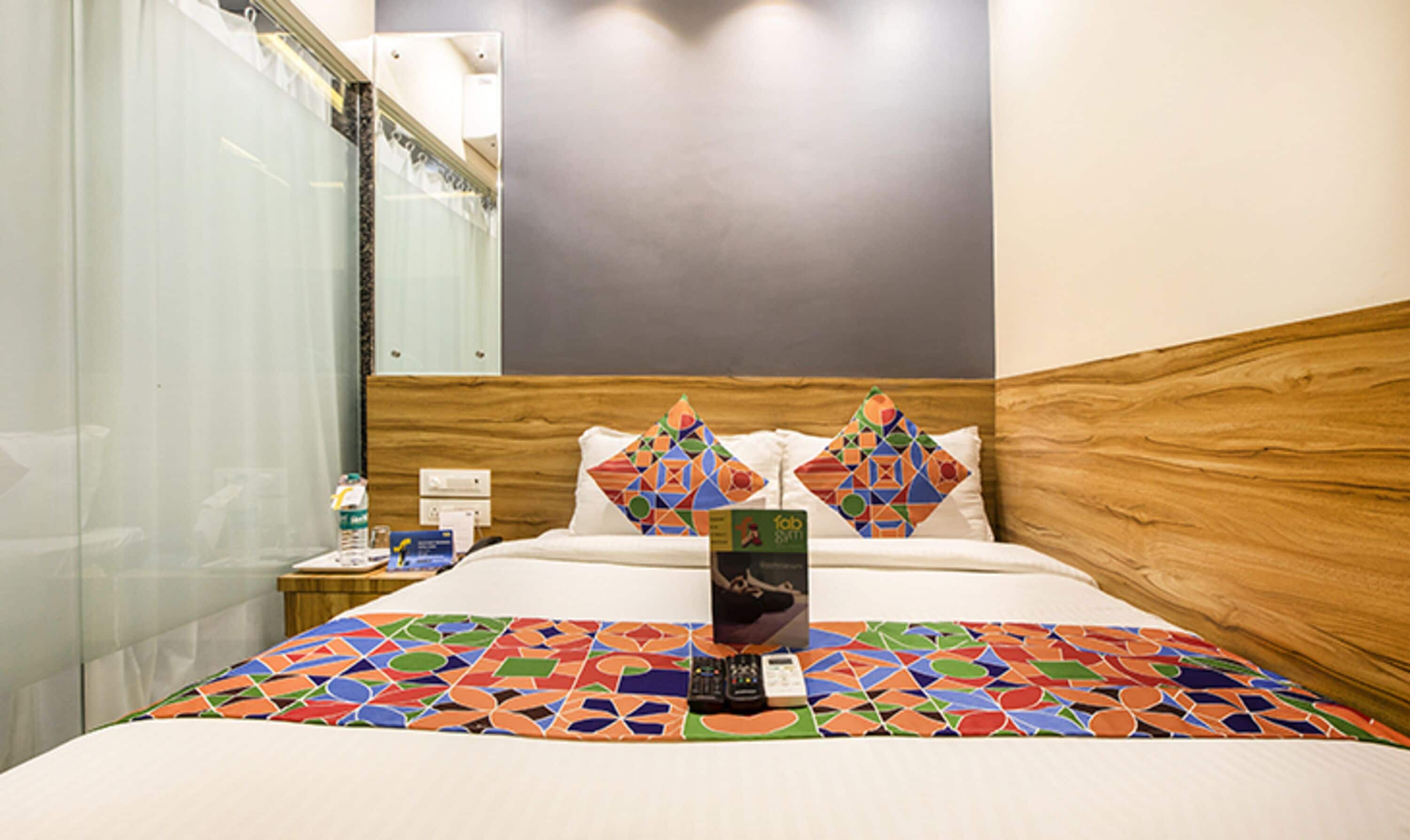 Habitación de hotel con cama, mesita de noche, espejo y ventana con cortinas.