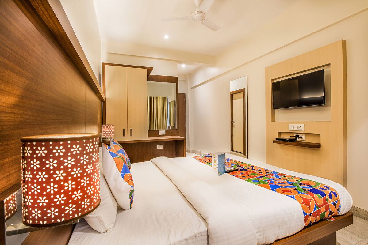 A hotel room with a bed, a TV mounted on the wall, a ceiling fan, and a wooden wardrobe.