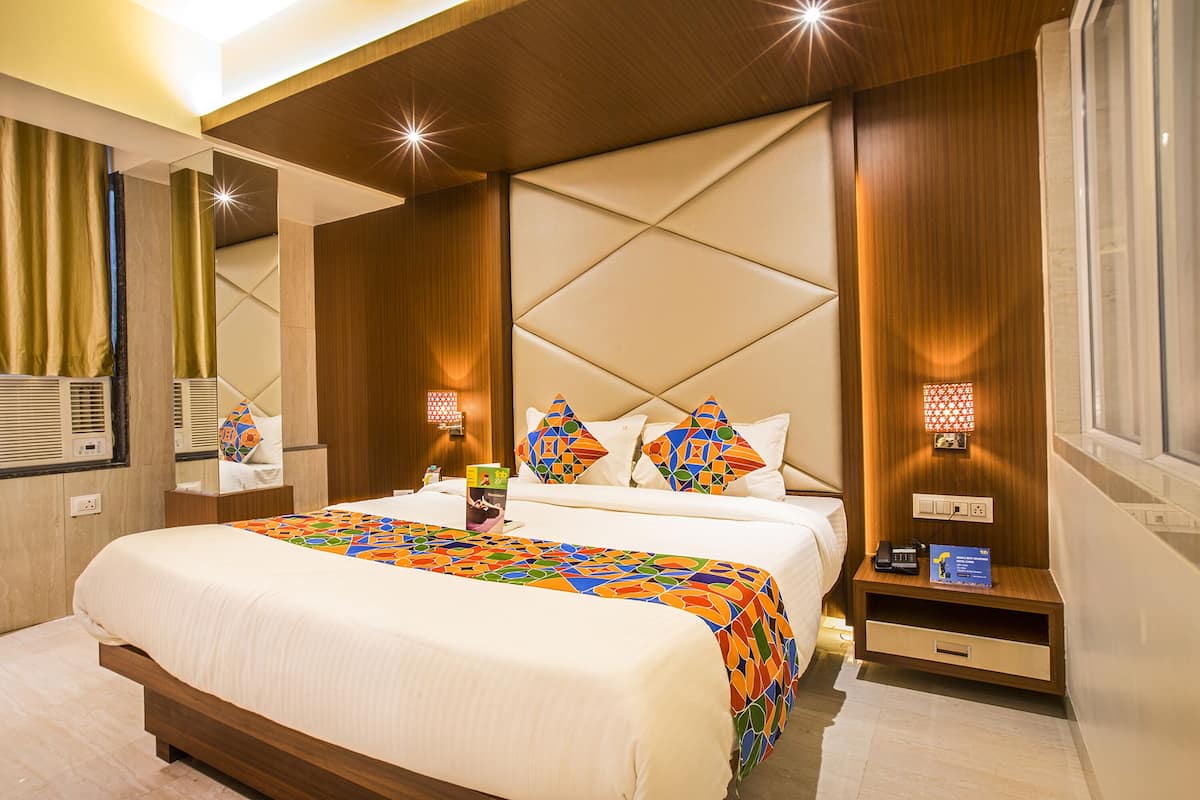 A modern hotel room with a large bed, a bedside table, a nightstand, and a mirror.