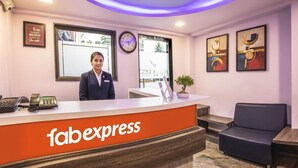 A reception area with a 'fabexpress' sign, a receptionist, a clock, framed artwork, and a plant. - FabHotel Silver Lake (Mumbai)
