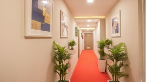 A hallway with a red carpet, framed artwork on the walls, and potted plants on either side. - FabHotel Silver Lake (Mumbai)