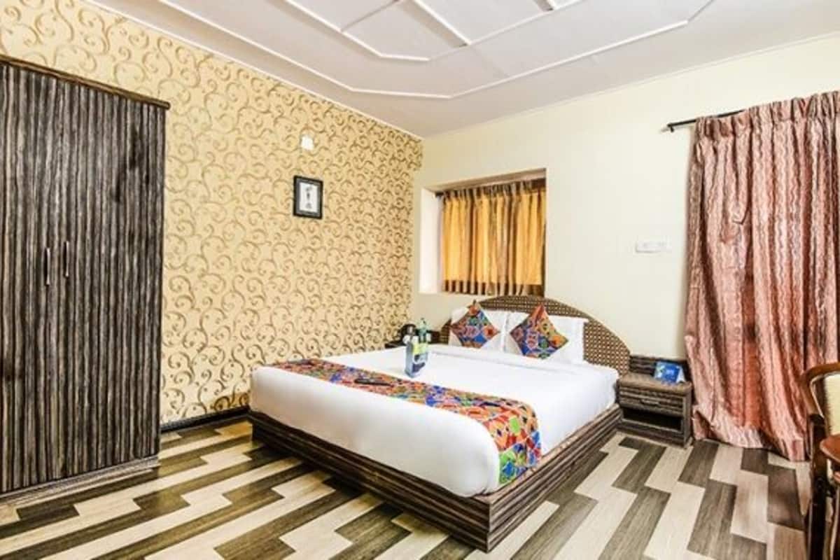 A hotel room with a bed, a wooden wardrobe, a small table, and a chair.