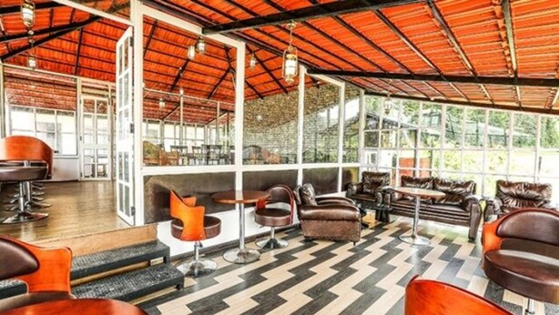 A spacious indoor area with a high ceiling, large windows, and a chevron-patterned floor. - Fabescape St. Clouds (Ootacamund)
