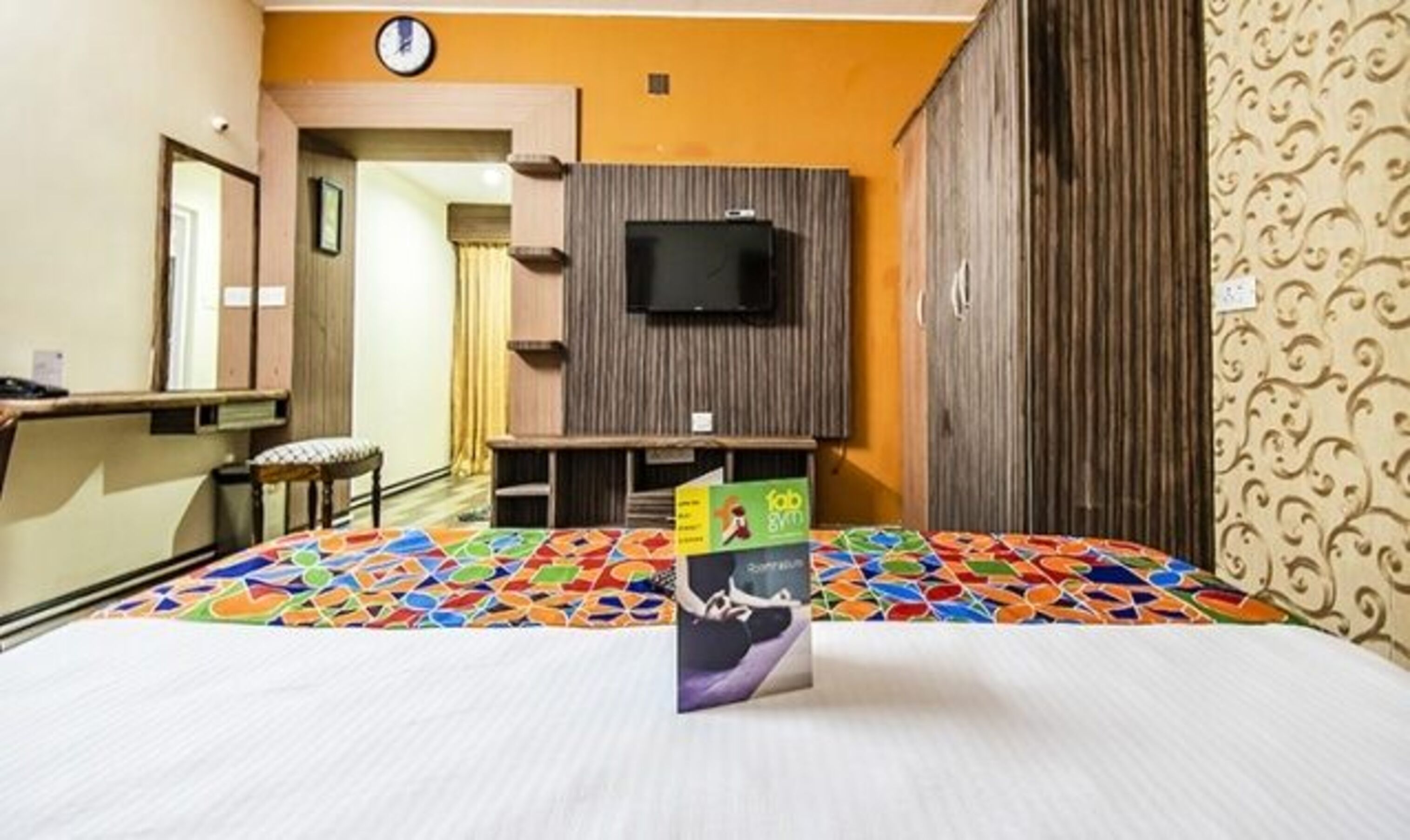 Una habitación de hotel con una cama, un televisor montado en la pared, un escritorio y una silla.
