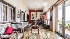A spacious living room with a sofa, armchairs, a coffee table, and a large window offering a view of the outdoors. - Fabescape St. Clouds (Ootacamund)