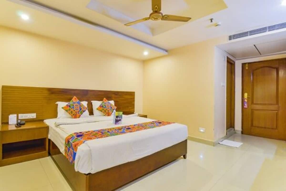 A hotel room with a wooden headboard, a bed with colorful bedding, a nightstand, a ceiling fan, and a door.