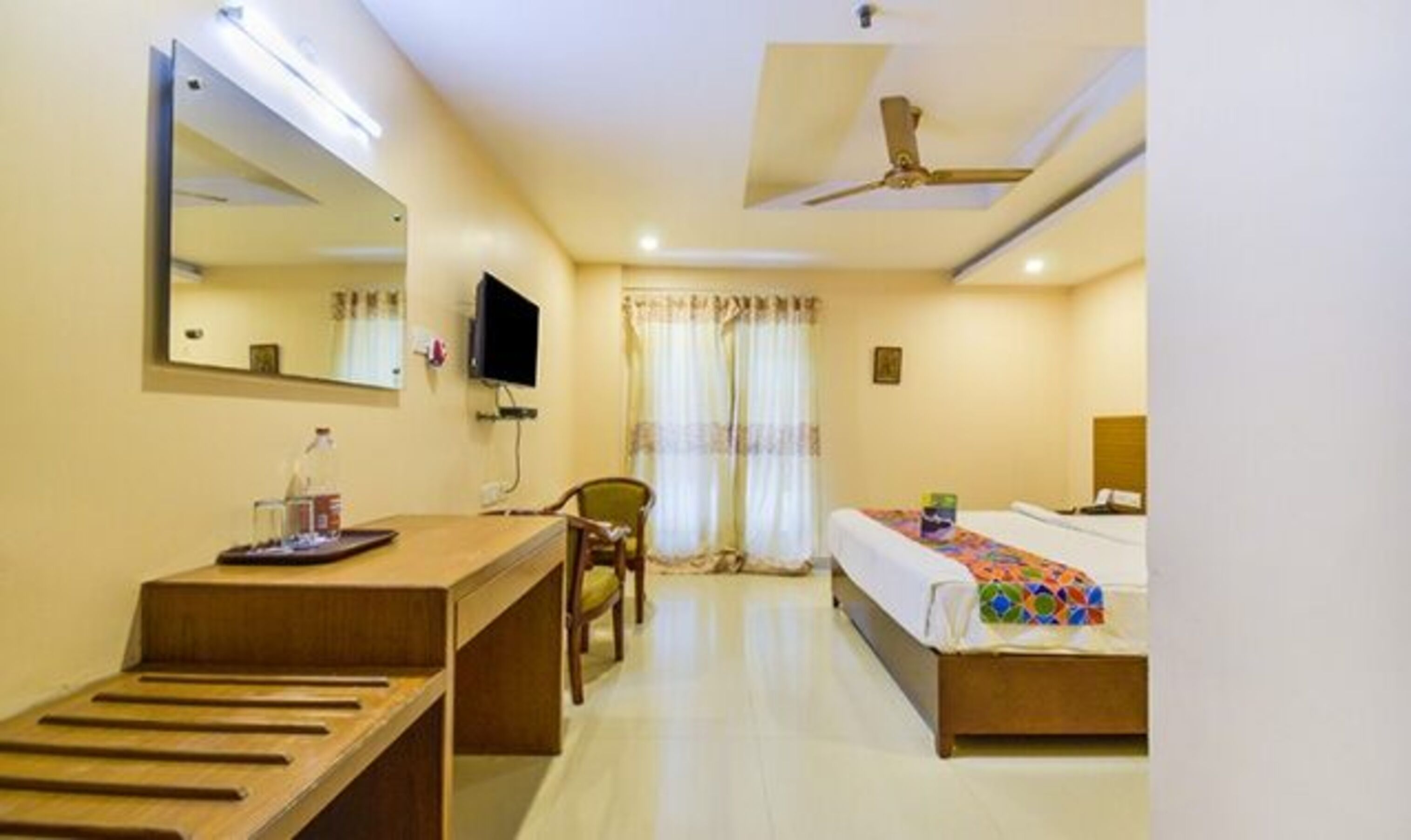 A hotel room with a desk, chair, bed, and a ceiling fan.