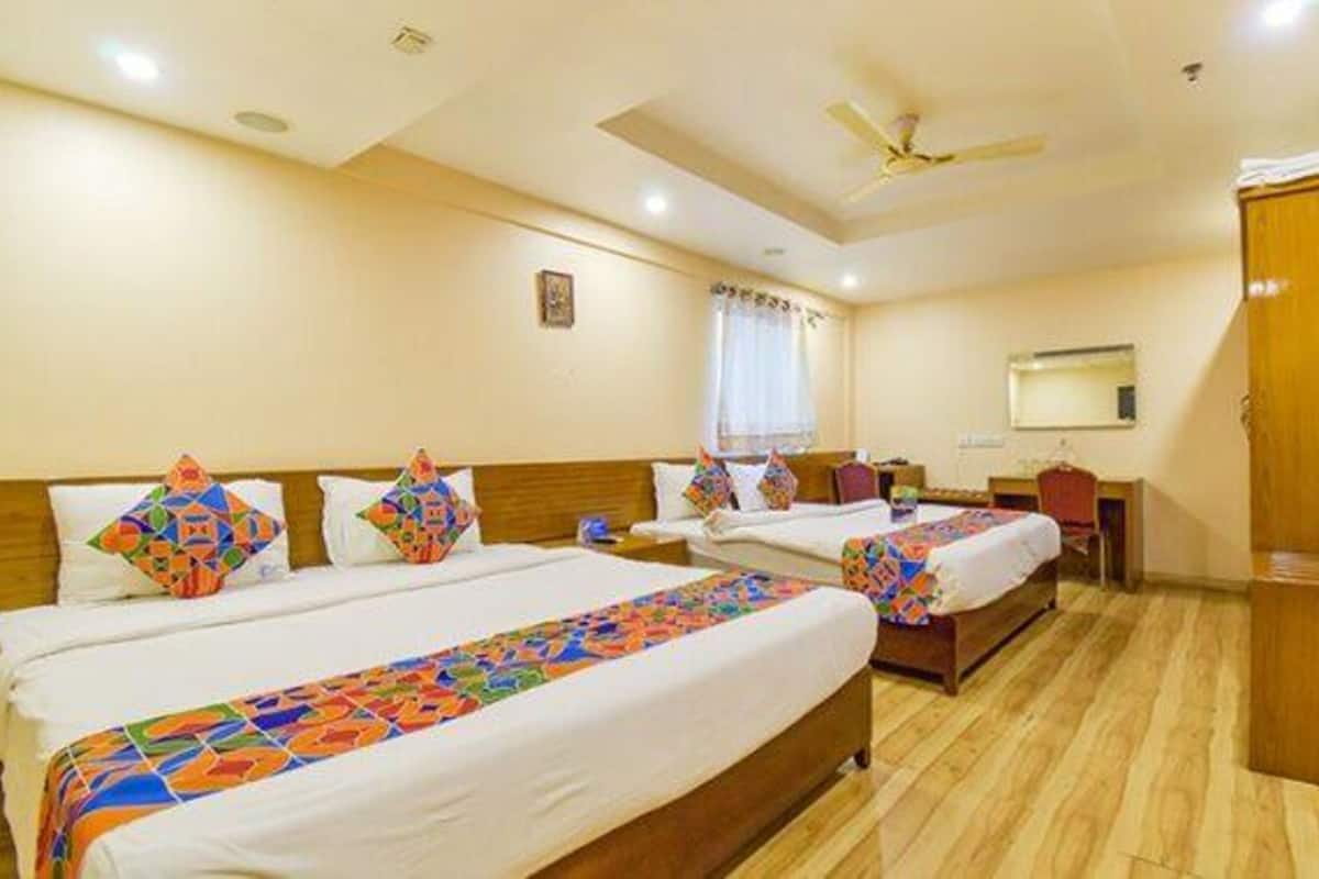 A hotel room with two beds, a desk, a wardrobe, and a ceiling fan.