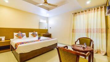 Une chambre d’hôtel avec un lit, une chaise, une table, un ventilateur de plafond et des rideaux.