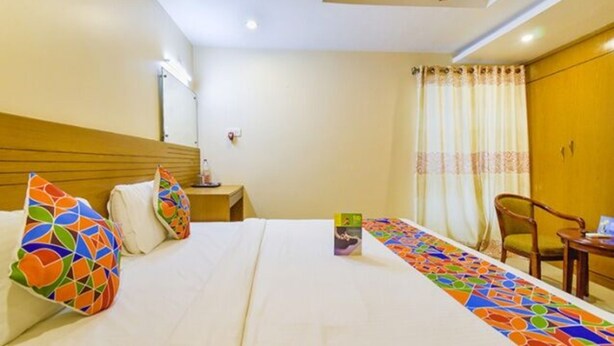 Una habitación de hotel con cama, mesita de noche, una silla y ventana con cortinas.