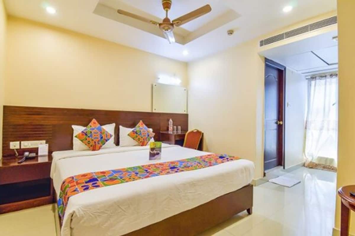 A hotel room with a large bed, a wooden headboard, a ceiling fan, and a nightstand with a lamp.