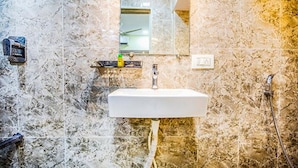 Un baño con pared de mármol, un lavabo blanco y un cabezal de ducha de mano.