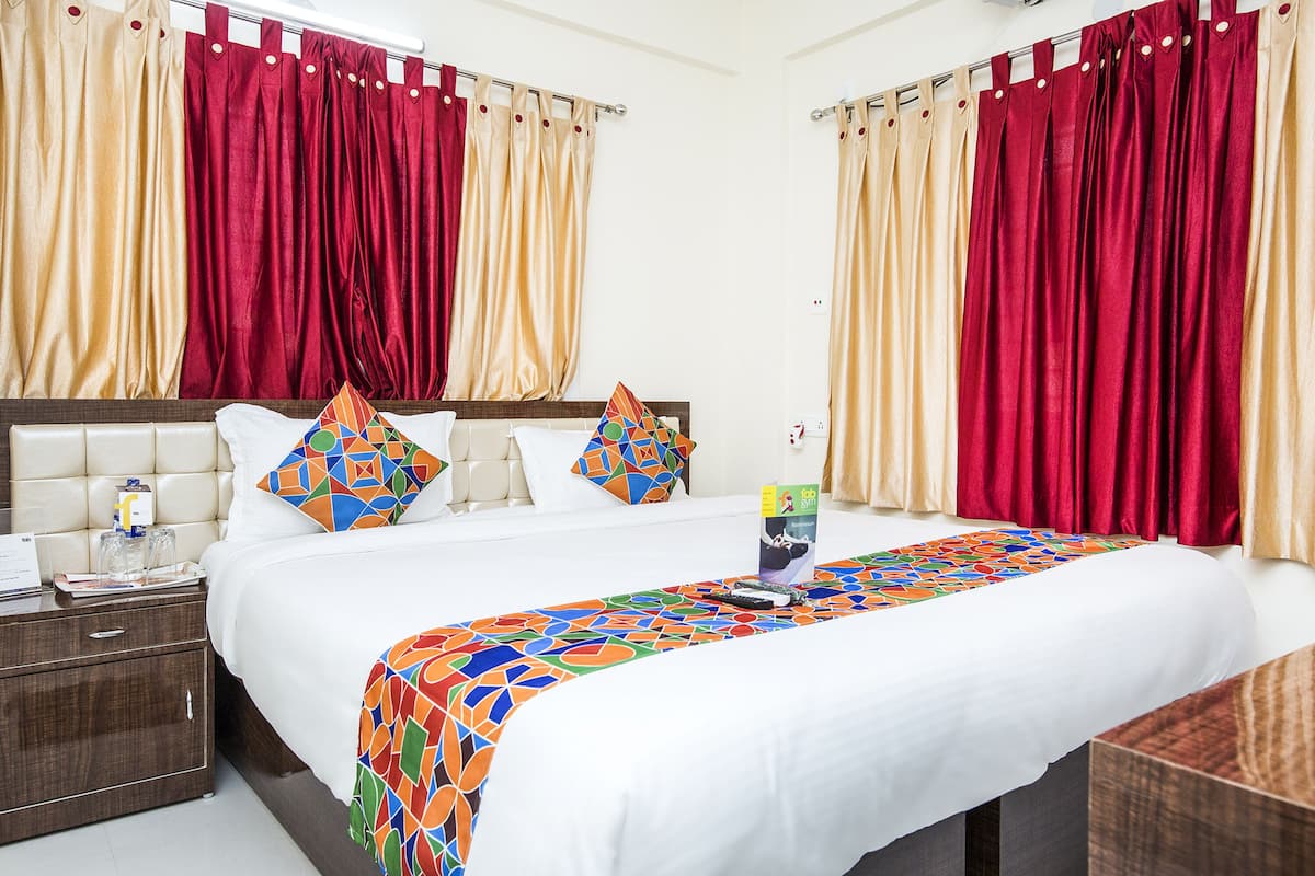 A hotel room with a large bed, two pillows, a bedside table with a lamp, and curtains.
