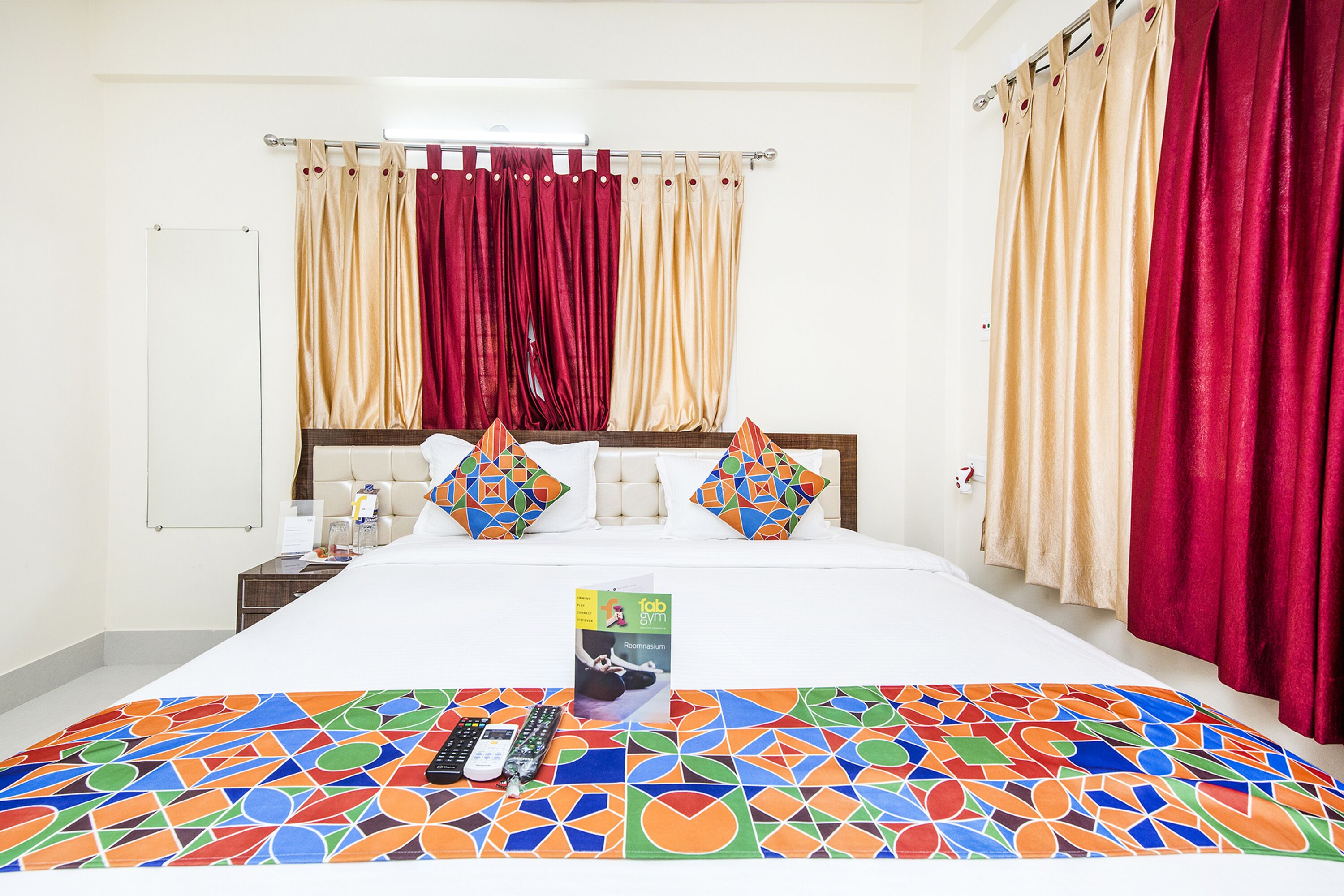 A hotel room with a large bed, two pillows, a bedside table, a nightstand, a colorful rug, and a book on the bed.